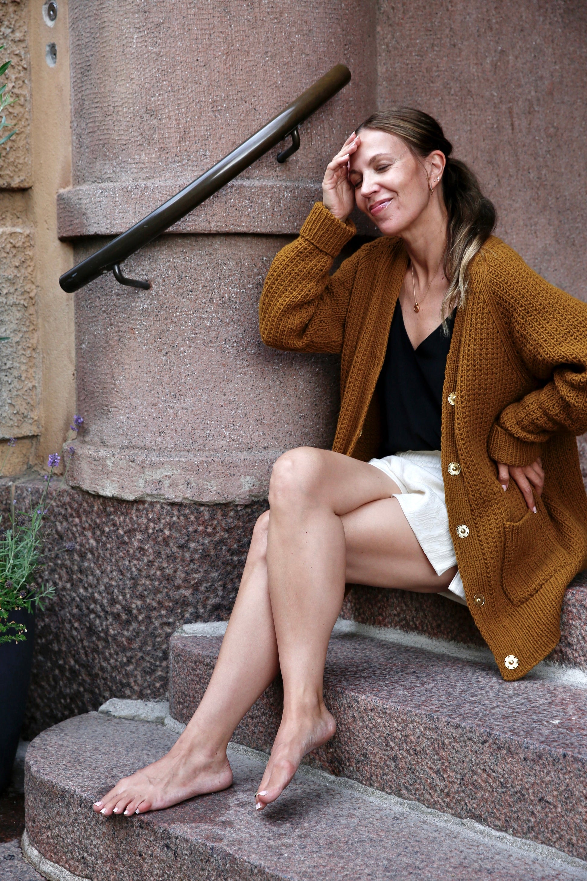 Cozy brown cardigan knitting pattern, close-up seated pose on stone steps